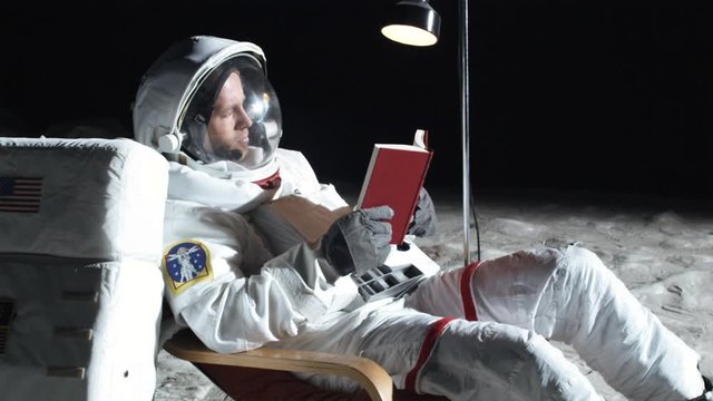SLO MO, MS, Lockdown, astronaut on the moon sitting in a reclining chair, reading a book