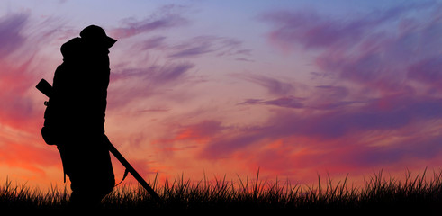 Silhouette of a hunter with a gun in the reeds against the sun, an ambush for ducks with dogs