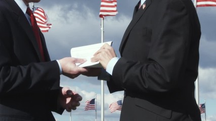CU of one man suspiciously passing a document another in front of American flags