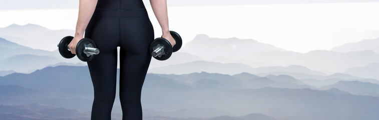 Fototapeta na wymiar A young slim athletic girl in sportswear performs a set of exercises on the background of mountains. Performs exercises with dumbbells. Fitness and healthy lifestyle.