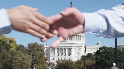 SLO MO, CU of two well-dressed men shaking hands in front of the Capitol Building, Washington DC