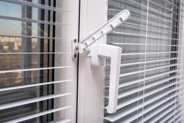 A handle and a restrictor, window stopper or limiter on PVC double glazed window with horisontal aluminium blinds close up
