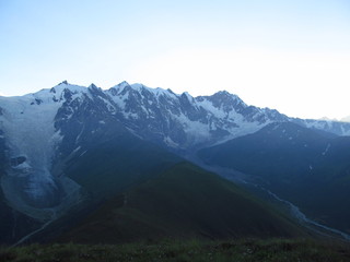 Mountain landscape of Svaneti on bright summer sunny day. Mountain lake, hills covered green grass on snowy rocky mountains background. Caucasus peaks in Georgia. Amazing view on wild georgian nature
