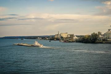 Shoreline Industry and Buildings and Tug Boat Pushing Sand Barges Down a River