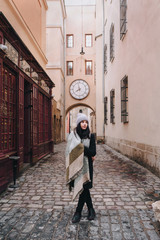 A young girl in coat, angora hat, wide scarf and autumn boots is walking along a narrow old street...