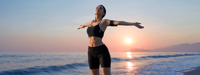 A thin athletic girl takes a break between classes on the background of the sunset by the sea in the early morning, enjoys silence and freedom.