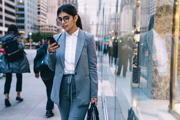 Young formal pretty businesswoman browsing smartphone on street