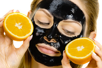 Girl black carbo mask on face holds orange fruit