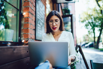 Surprised hipster girl in spectacles making online booking during leisure time for distance job, attractive woman in eyewear reading shocked news about 5 generation for internet virtual connection