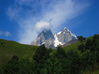 Naklejka premium Mountain landscape of Svaneti on bright summer sunny day. Mountain lake, hills covered green grass on snowy rocky mountains background. Caucasus peaks in Georgia. Amazing view on wild georgian nature
