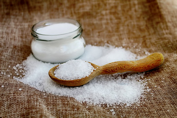 Coarse salt on a vintage handmade wooden spoon and fine salt in a glass jar on old fabric