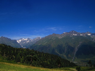 Mountain landscape of Svaneti on bright summer sunny day. Mountain lake, hills covered green grass on snowy rocky mountains background. Caucasus peaks in Georgia. Amazing view on wild georgian nature