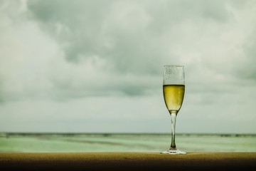 A glass of champagne on a wooden surface, with tranquil seas and the Maldivian coastline in the background, capturing a moment of luxury and relaxation.