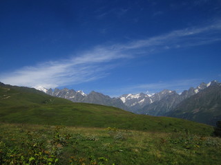 Mountain landscape of Svaneti on bright summer sunny day. Mountain lake, hills covered green grass on snowy rocky mountains background. Caucasus peaks in Georgia. Amazing view on wild georgian nature