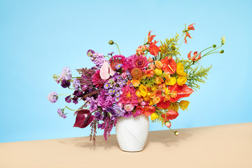 Contemporary Floral Arrangement with Anthurium Dahlia flowers in vase on table top with solid colors