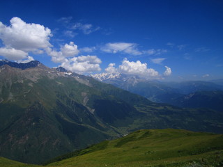 Mountain landscape of Svaneti on bright summer sunny day. Mountain lake, hills covered green grass on snowy rocky mountains background. Caucasus peaks in Georgia. Amazing view on wild georgian nature