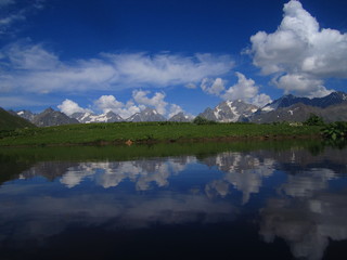 Mountain landscape of Svaneti on bright summer sunny day. Mountain lake, hills covered green grass on snowy rocky mountains background. Caucasus peaks in Georgia. Amazing view on wild georgian nature