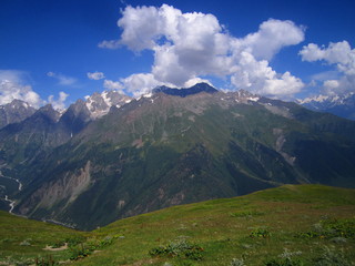 Mountain landscape of Svaneti on bright summer sunny day. Mountain lake, hills covered green grass on snowy rocky mountains background. Caucasus peaks in Georgia. Amazing view on wild georgian nature