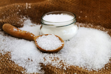 Coarse salt on a vintage handmade wooden spoon and fine salt in a glass jar. Background - fabric,...