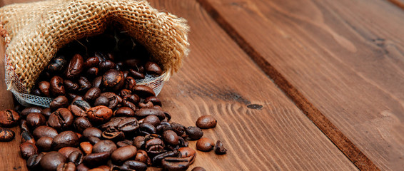 Fresh roasted coffee beans falling out the sack on the wooden surface. Brown coffee beans scattered from bag on the table