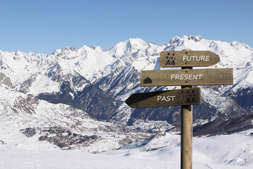 three signs indicating the way to the past, present and future over the mountains covered of snow