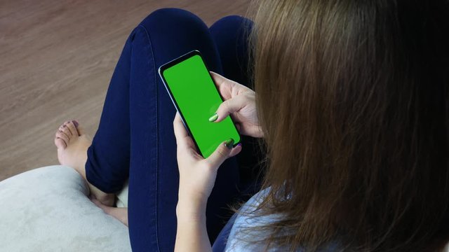 Woman at home relaxing reading on the smartphone with pre-keyed green screen
