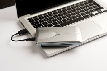 Aluminum external hard drive, with cable (usb) on top of laptop, on the white office table. 