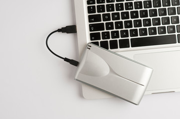Aluminum external hard drive, with cable (usb) on top of laptop, on the white office table. Top view