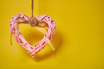 decorative pink heart made of branches with woolen thread. pendant decoration on the right on a yellow background. Valentine's Day