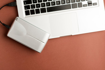 Aluminum external hard drive with cable (usb) connected to laptop, on brown office table.Top view