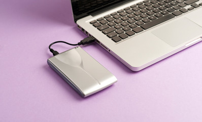 Aluminum external hard drive, partial laptop view, purple background, office concept.