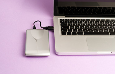 Aluminum external hard drive, laptop, purple background, office concept.