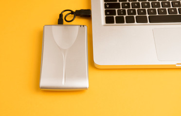 Aluminum external hard drive, partial laptop view, on orange office table.Top view