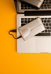 Aluminum external hard drive, partial laptop view, on orange office table.Top view