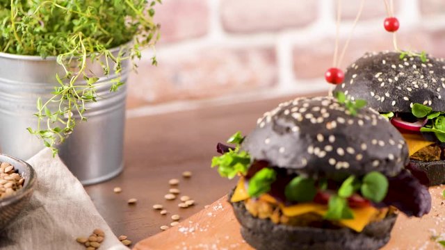 Tasty grilled veggie burger with lentils, dry tomato and thyme with black bread on wooden countertop.