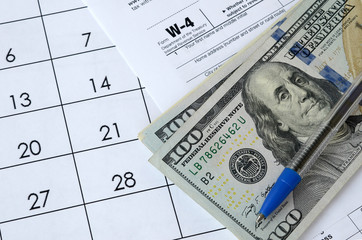 Form W-4 Employee's withholding allowance certificate and blue pen with dollar bills lies on office...