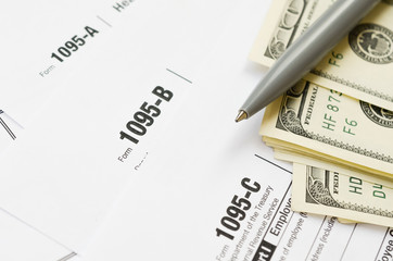IRS Form 1095-A 1095-B and 1095-C blank lies on empty calendar page with pen and dollar bills