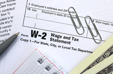 The pen, notebook and dollar bills is lies on the tax form W-2 Wage and Tax Statement. The time to...
