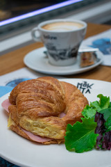 Croissant de jamón con ensalada a un lado y café de fondo