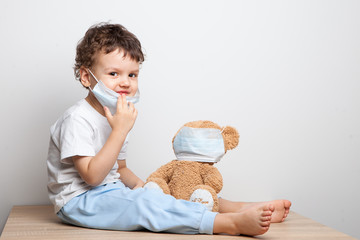 teaching your child preventive measures against viruses and flu. baby, boy in a medical mask puts a medical mask on his teddy bear toy. care for loved ones. Basic hygiene rules