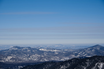Obraz na płótnie Canvas Winter mountain landscape. Snow-capped mountains overgrown with taiga against a blue sky. Russia. Altai Republic.
