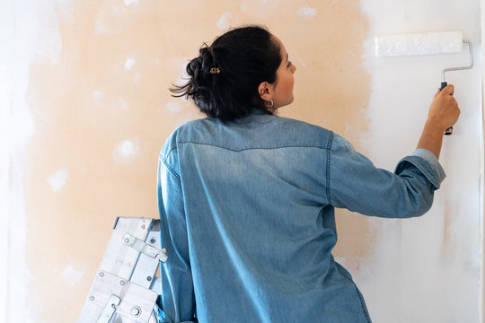 Brunette woman painting a wall on white with a paint roller