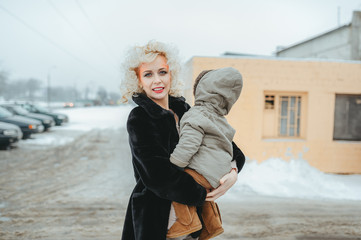 Portrait of young blonde mother holding little son in street in winter