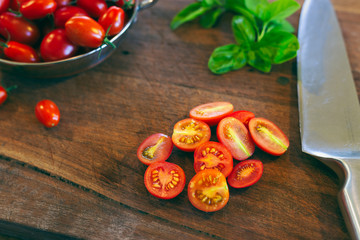 Sliced cherry tomatoes and fresh basil on a rustic timber chopping black with knife in organic...