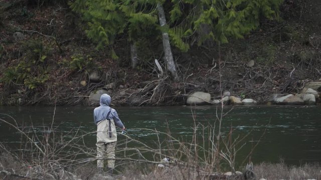 Male in waders alone fishing peacefully casting pole lure on river water bank on sandy river in pacific northwest oregon wide angle in slow motion