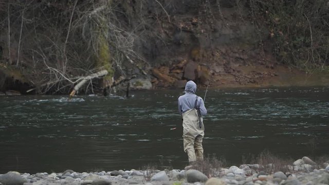 Male in waders alone fishing peacefully casting fishing pole lure on river water bank on sandy river in pacific northwest oregon wide angle in slow motion
