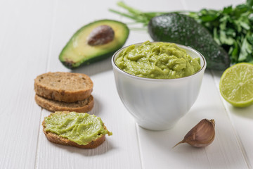 Freshly made guacamole in a white Cup and on slices of bread. Diet vegetarian Mexican food avocado.