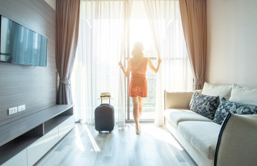Tourist woman looking to beautiful view with her luggage in hotel living room.