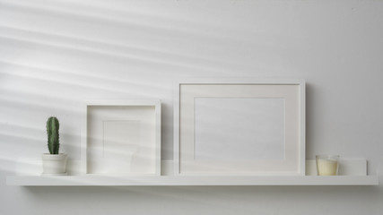 Close up view of mock up frames and decorations on white shelf with white wall background