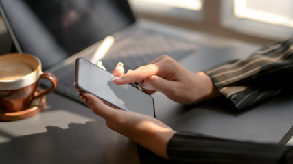 Obraz na płótnie Canvas Cropped shot of businesswomen texting on blank screen smartphone in modern dark office room